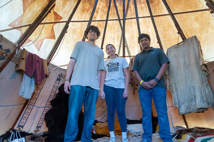 3 students stand inside of a tee pee.